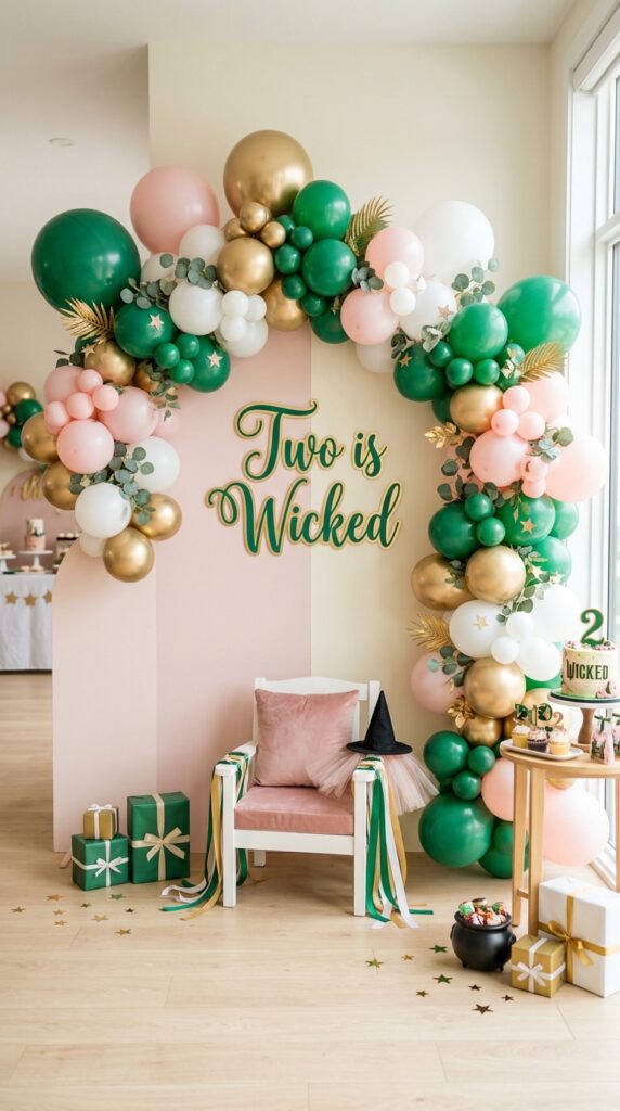Emerald green and pink Wicked-themed 2nd birthday balloon backdrop with gold accents and photo area.